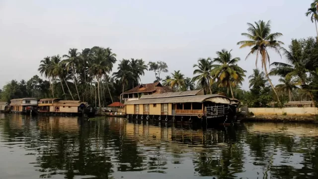 Traditional houseboat moving through Alleppey backwaters with village life along the canal