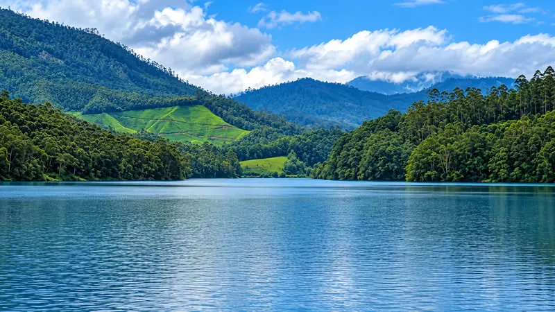 Calm blue water at Kundala Reservoir surrounded by wooded hills and tea plantations.